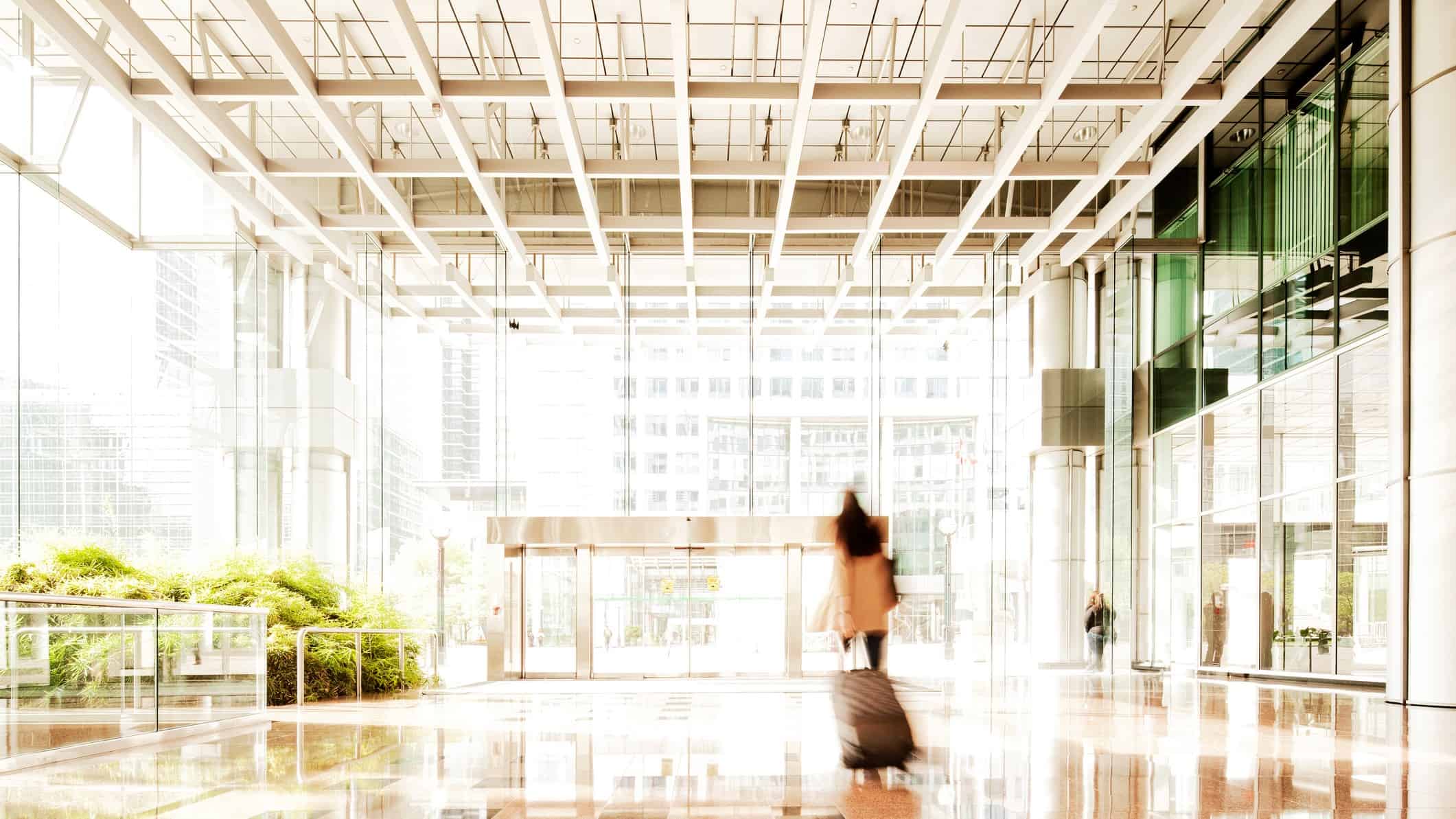 A lone traveller walks a suitcase through a large, empty airport terminal.