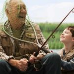 A young boy laughs with his grandpa as he puts a fishing net over his head.