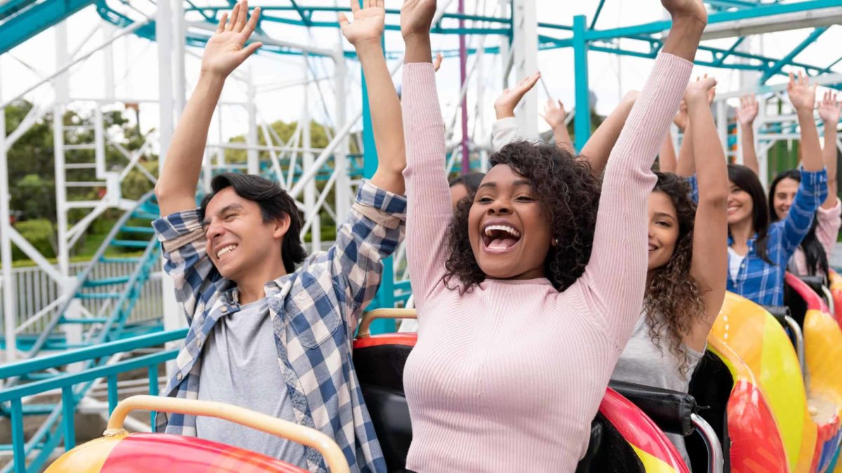 two people sit side by side on a rollercoaster ride with their hands raised in the air and happy smiles on their faces