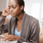 a woman sits with a concerned look on her face at her computer a home office environment.