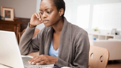 a woman sits with a concerned look on her face at her computer a home office environment.