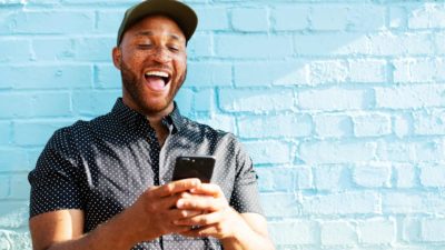 a man looks down at his phone with a look of happy surprise on his face as though he is thrilled with good news.