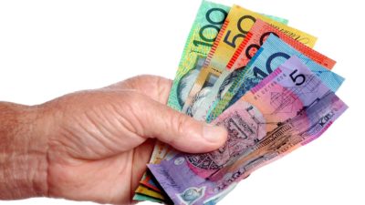 a hand reaches out with australian banknotes of various denominations fanned out.