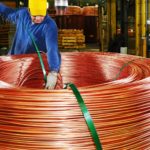 Two workers working with a large copper coil in a factory.