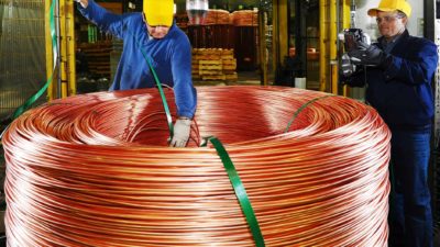 A worker stands over a large copper coil in a factory