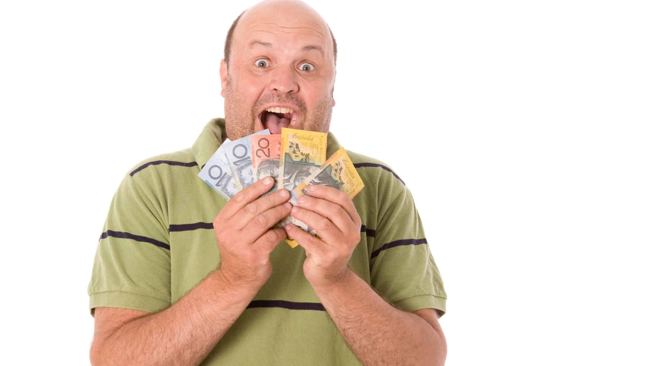 a man wearing casual clothes fans a selection of Australian banknotes over his chin with an excited, widemouthed expression on his face.