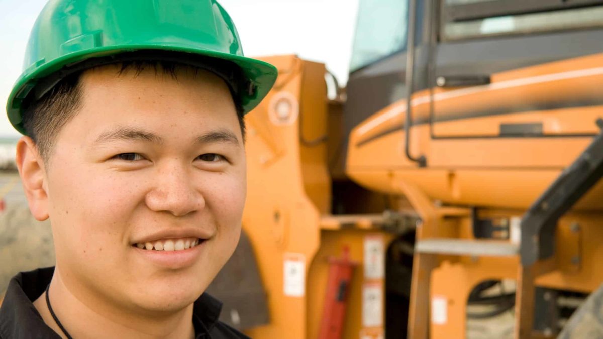 a miner with a green hard hat stands in front of a piece of heavy mining equipment.