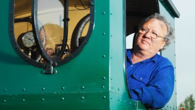 a train driver leans out of the window of a green locomotive train.