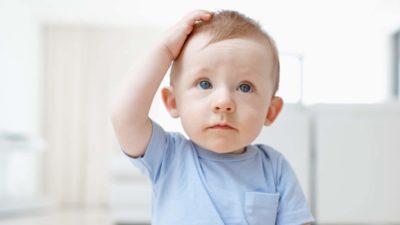 a baby scratches his head looking slightly bemused.