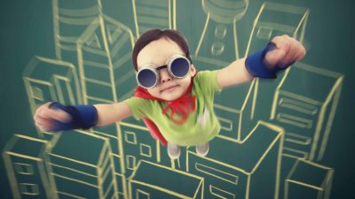 a small boy dressed in a superhero outfit soars into the sky with a graphic backdrop of a cityscape.