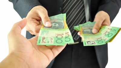 A man in a business suit whose face isn't shown hands over two australian hundred dollar notes from a pile of notes in his other hand to an outstretched hand of another person.