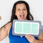 A smiling woman holds an arm in the air in triumph while also holding a graphic of a fully-charged battery in her other hand representing the Pilbara Minerals share price