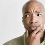 a man holds his hand to his chin with a furrowed brow, making an expression of puzzlement or confusion.