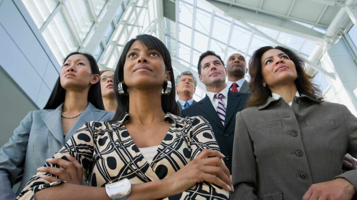 A group of businesspeople stand side by side, looking up, with serious but satisfied expressions on their faces.