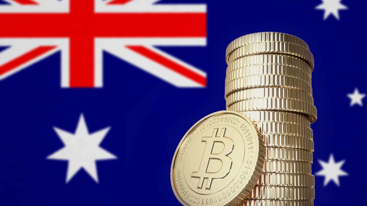 a pile of bitcoins with a bitcoin resting against it stands in front of an Australian flag.