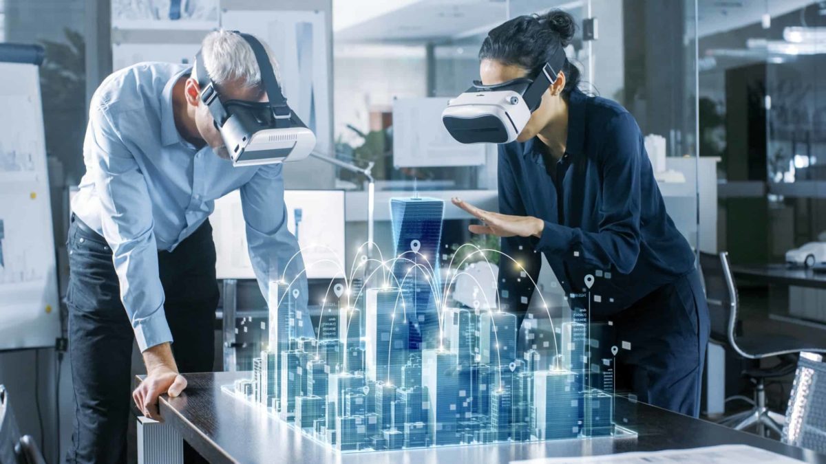 two people wearing virtual reality goggles look over a 3D model of a city created using digital technology.