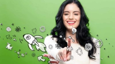 A woman on a green background points a finger at graphic images of molecules, a rocket, light bulbs and scientific symbols as she smiles.