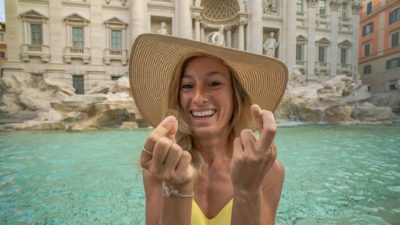 A woman crosses her fingers as she flicks a coin into a fountain, hoping for good luck.