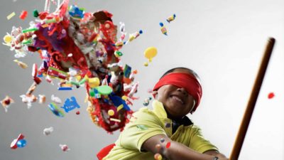 A young boy wearing a red blindfold knocks the stuffing out of a pinata.