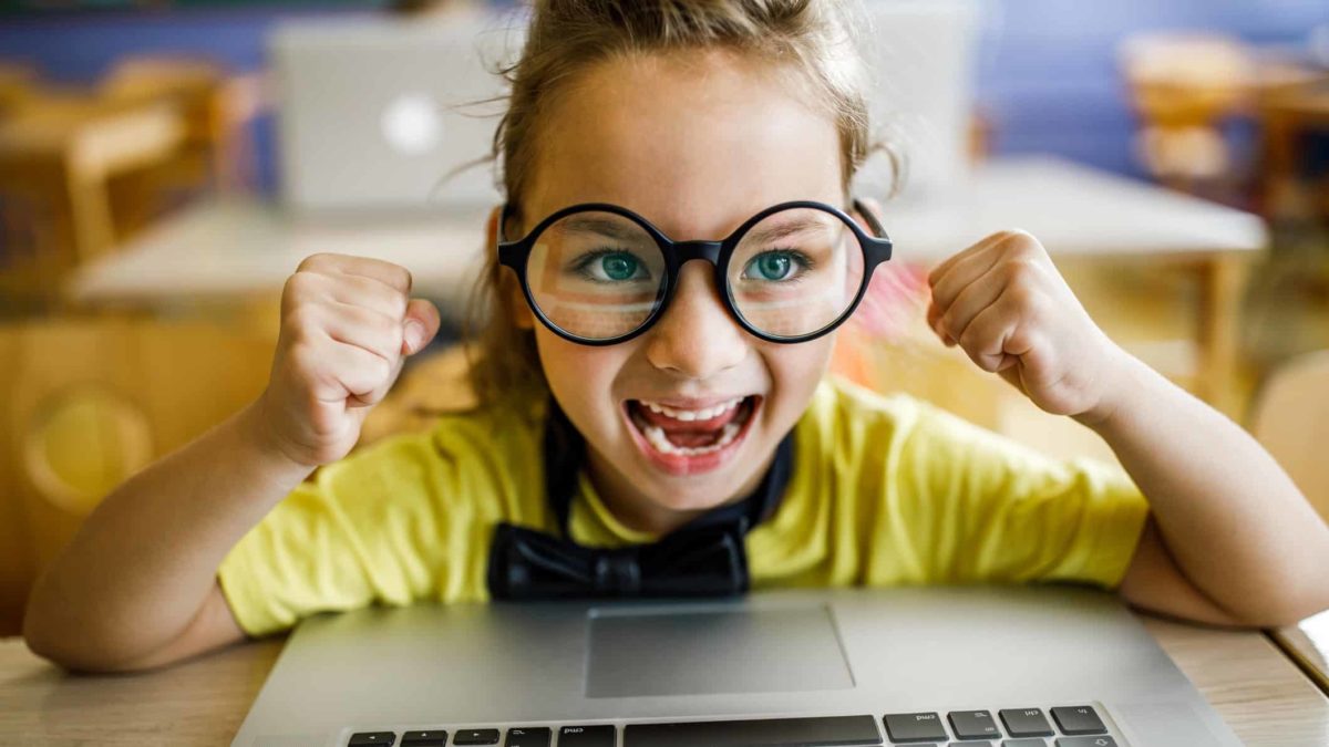 Little girl with big glasses on a laptop with a big smile on her face.