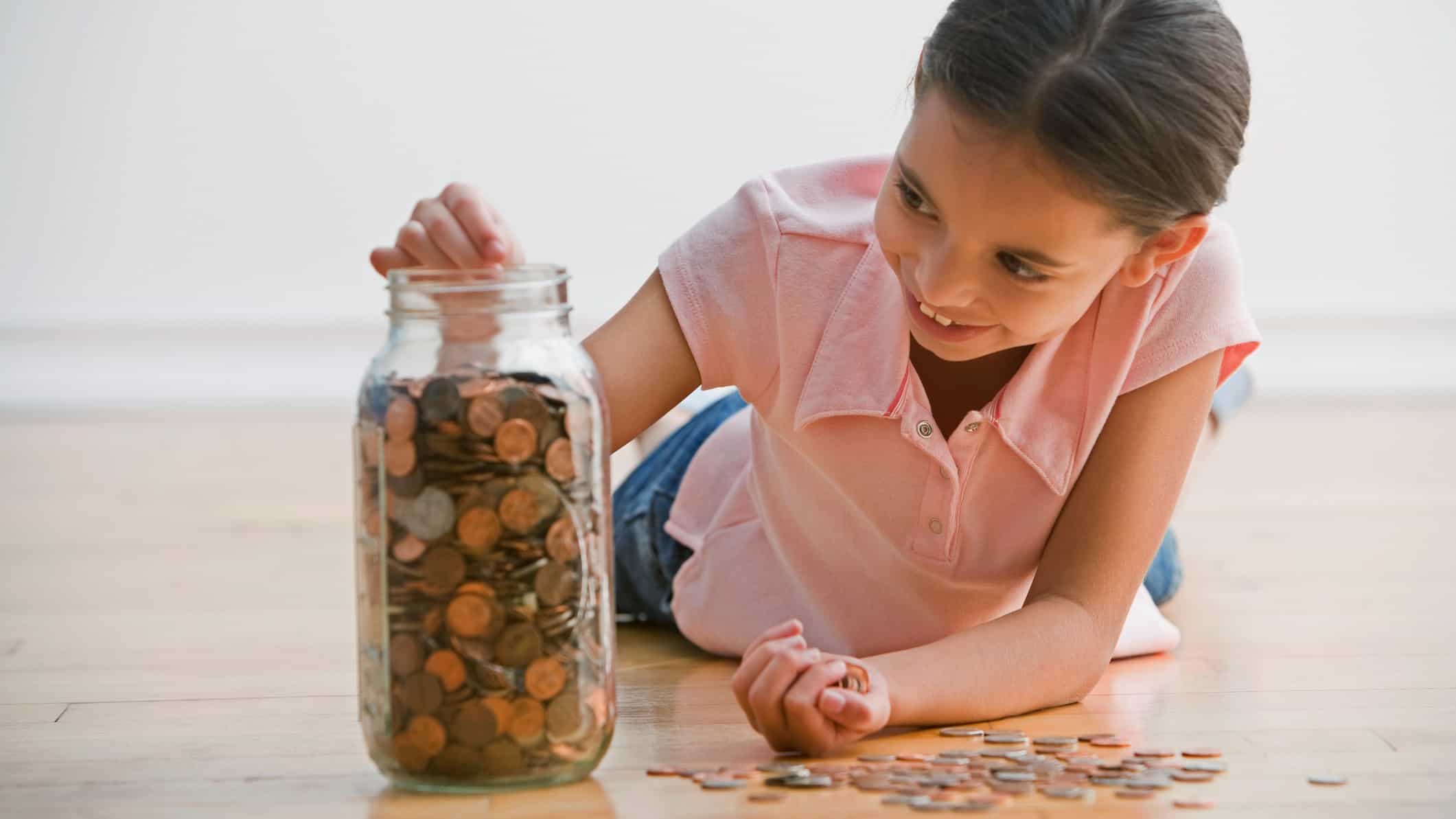 A little girl fills her jar up with coins with a smile on her face.