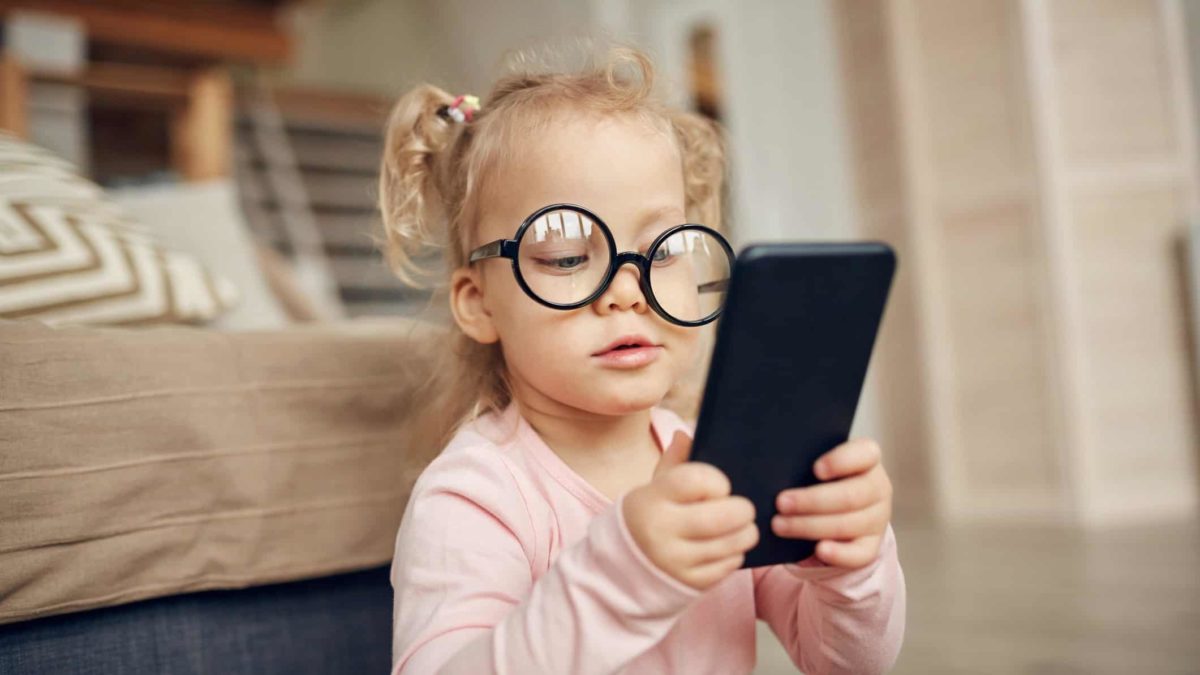 A little girl wearing wonky glasses checks out what's happening in the world on a mobile phone.