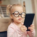 A little girl wearing wonky glasses checks out what's happening in the world on a mobile phone.