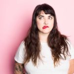 A woman with red lipstick and tattoos pulls a face as though the situation is not looking good.