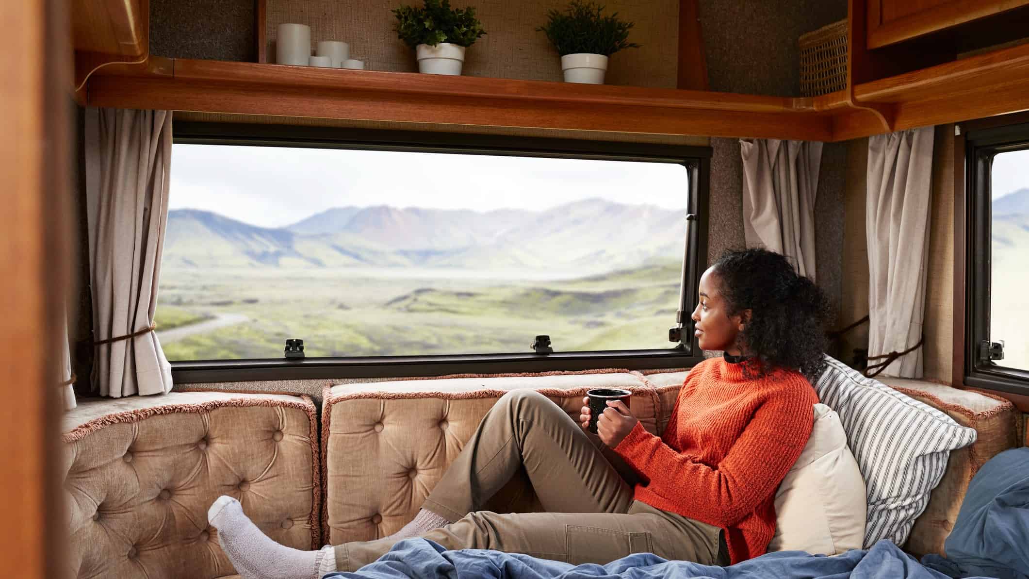 A young woman sits on her bed holding a cup of coffee inside her recreational vehicle hired through the Camplify website