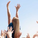 A woman stretches her arms into the sky as she rises above the crowd.