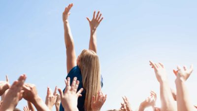 A woman stretches her arms into the sky as she rises above the crowd.