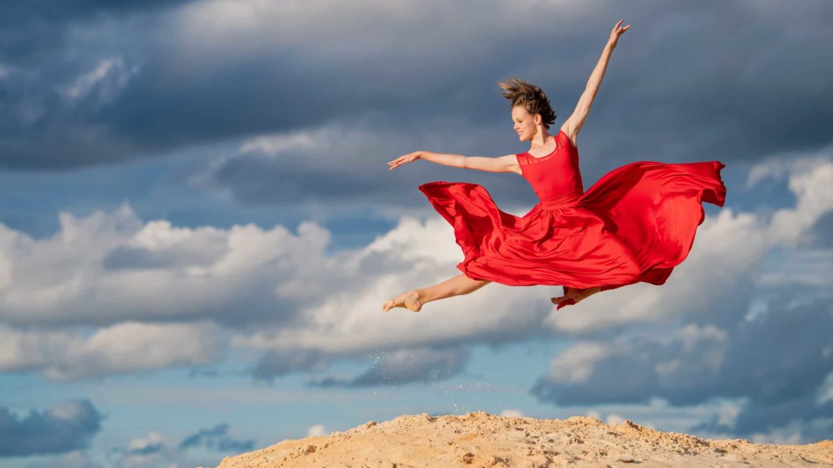 A female dancer dressed in red soars over the earth after taking a giant leap.