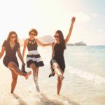 Three women dance and splash about in the shallow water of a beautiful beach on a sunny day.