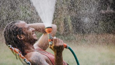 A guy reclines in his backyard spraying water from the hose all over himself.