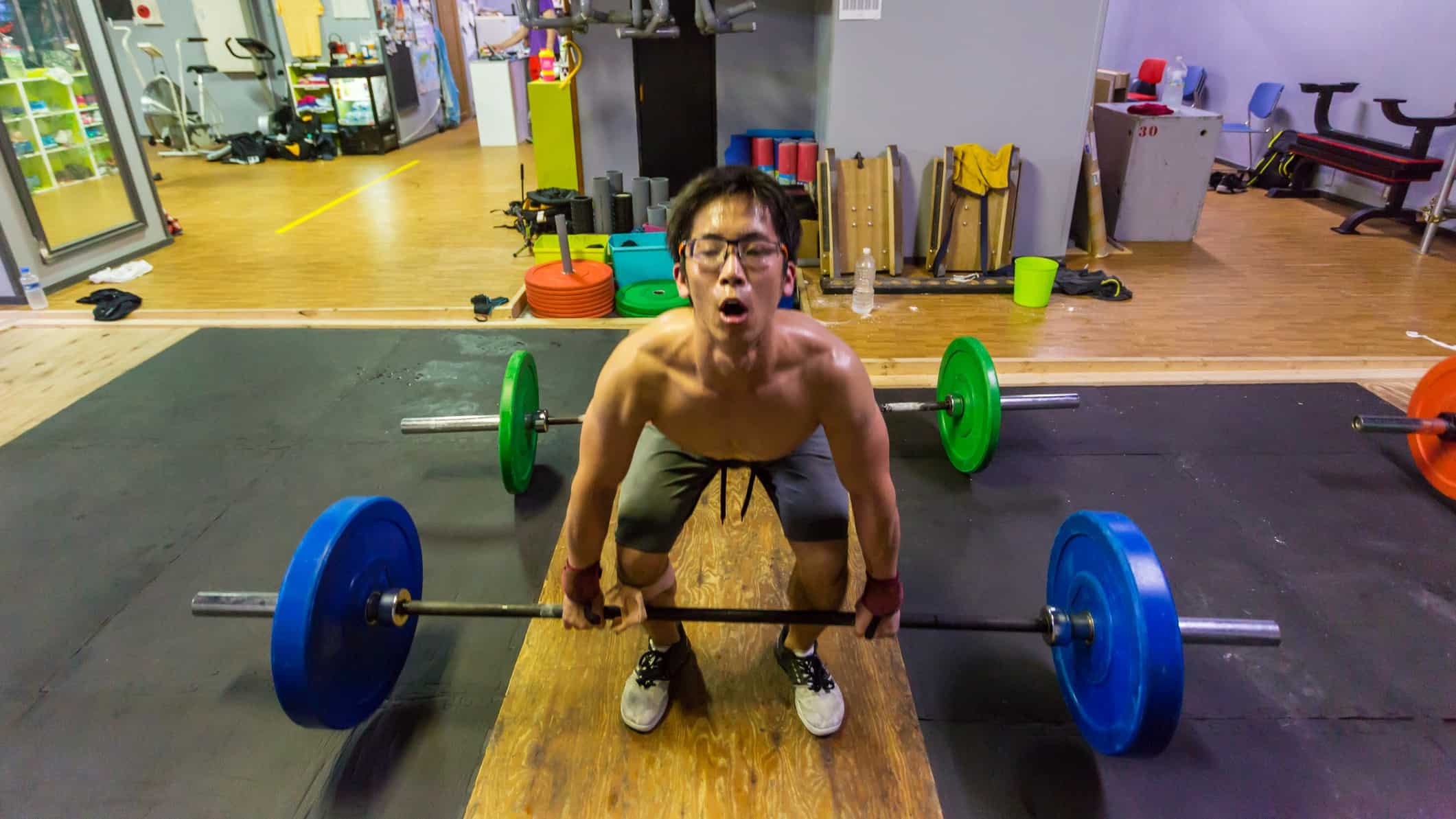 A weightlifter struggles to lift a heavy iron barbell off the ground.
