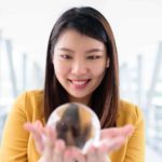 A woman gazes with anticipation into a glass ball she's holding in her hands.