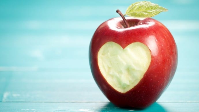 an apple with a leaf on its stem has a heart shaped bit taken from it