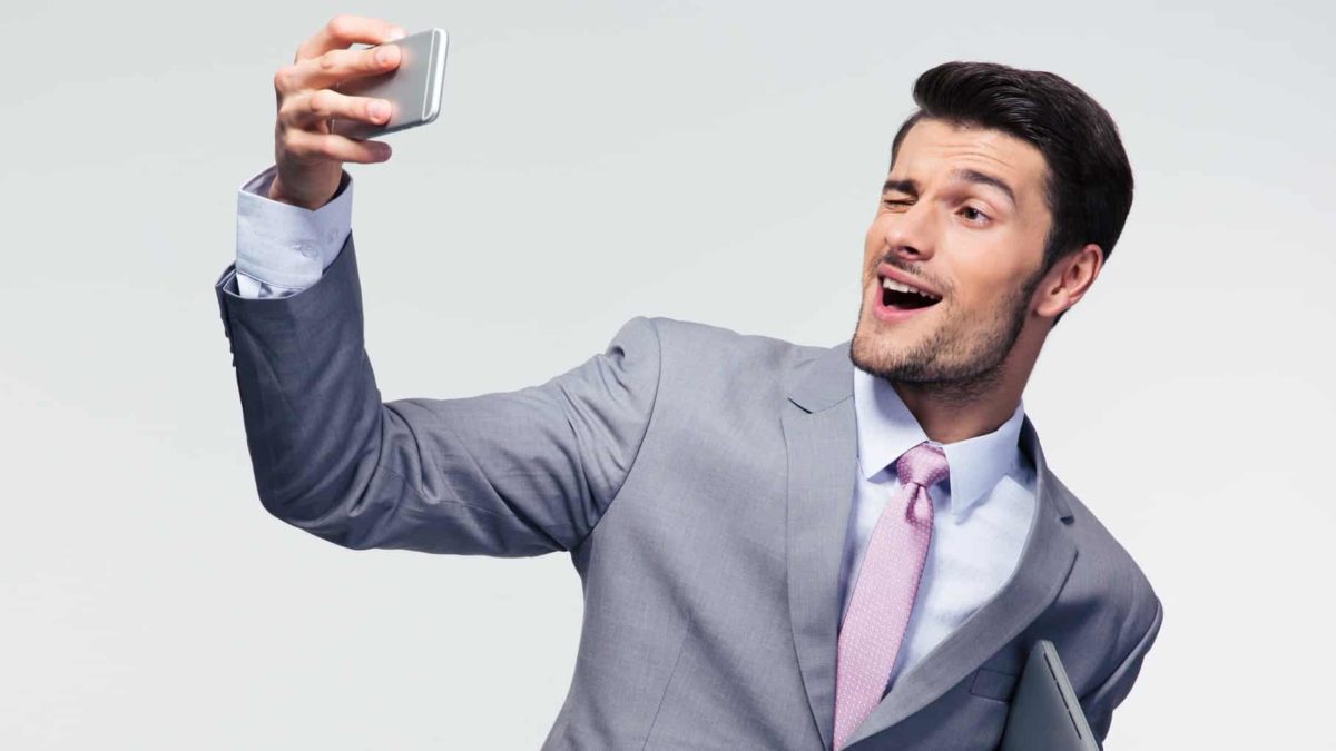 An arrogant banker pleased with himself and his success winks at his mobile phone while taking a selfie