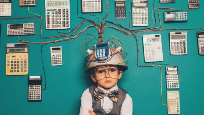 A youngA young boy dressed as a nerd wears a makeshift helmet and invention which uses many calculators to compute his solutions.
