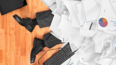 A pair of legs can be seen on the floor buried under a pile of paperwork, indicating a high volume day.