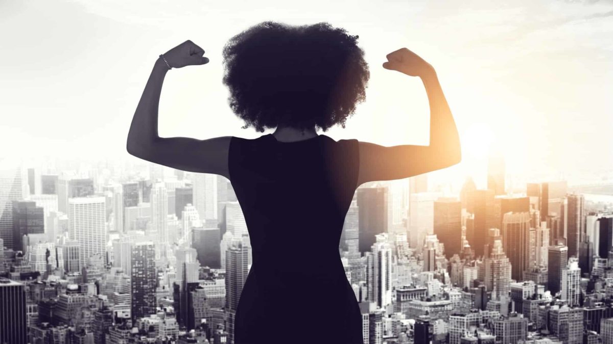 A business woman flexes her muscles overlooking a city scape below.