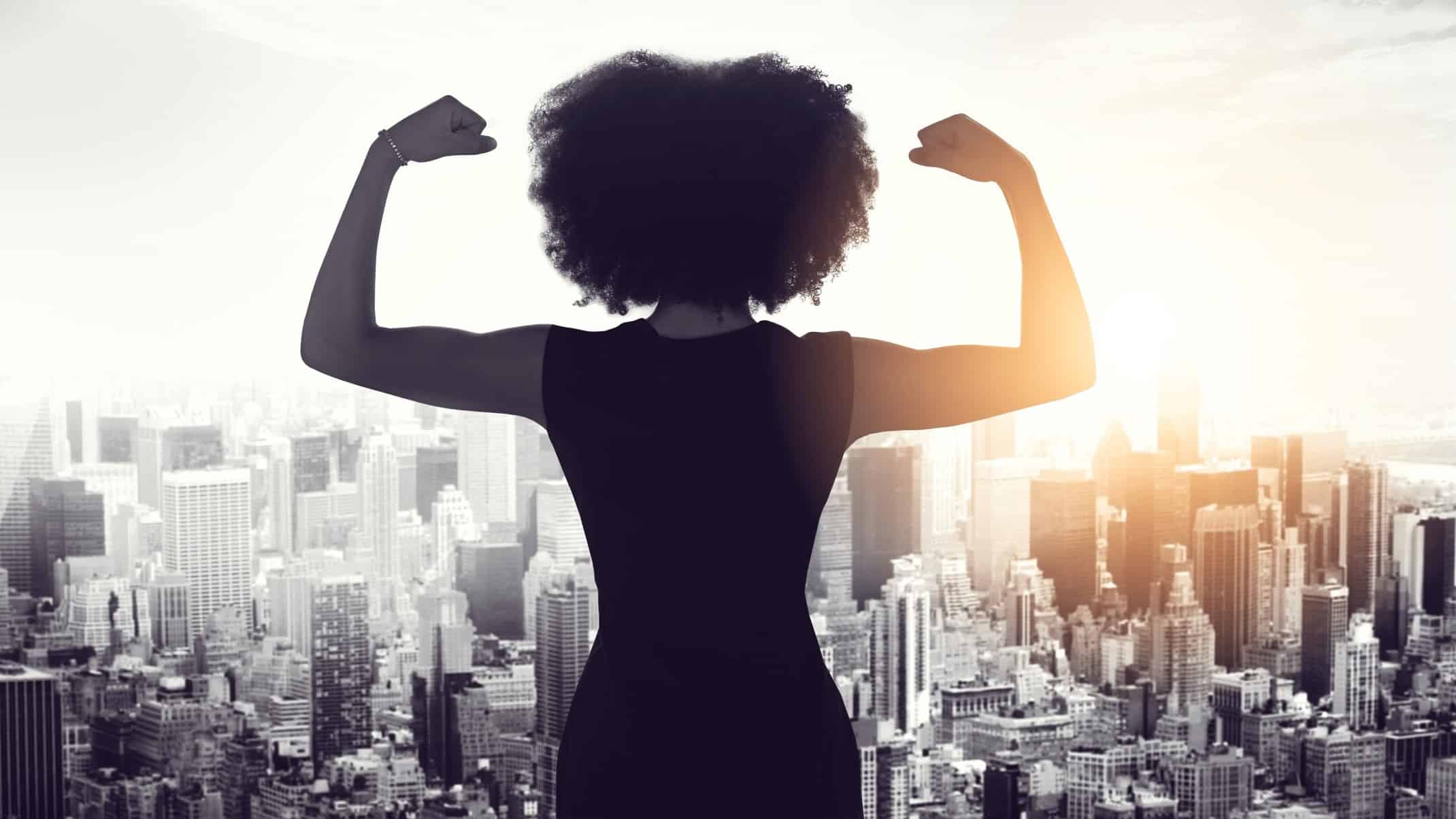 A business woman flexes her muscles overlooking a city scape below