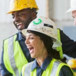 One female and two male construction workers laugh on site.