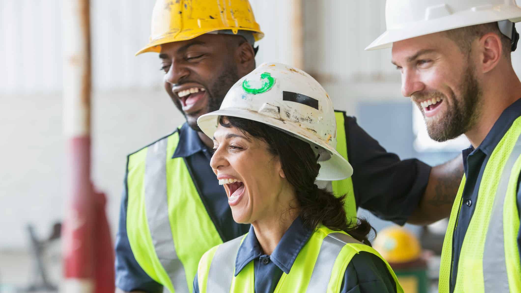 One female and two male construction workers laugh on site.