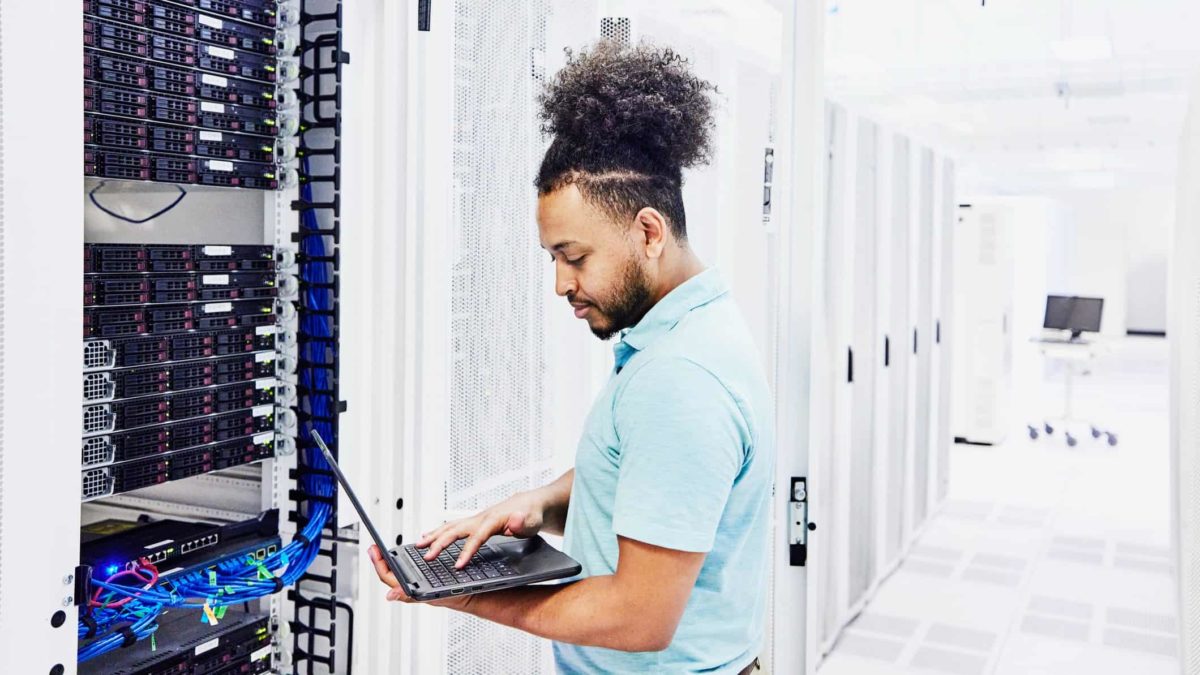 Cybersecurity company employee looks at laptop while standing near server room
