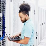 Cybersecurity company employee looks at laptop while standing near server room