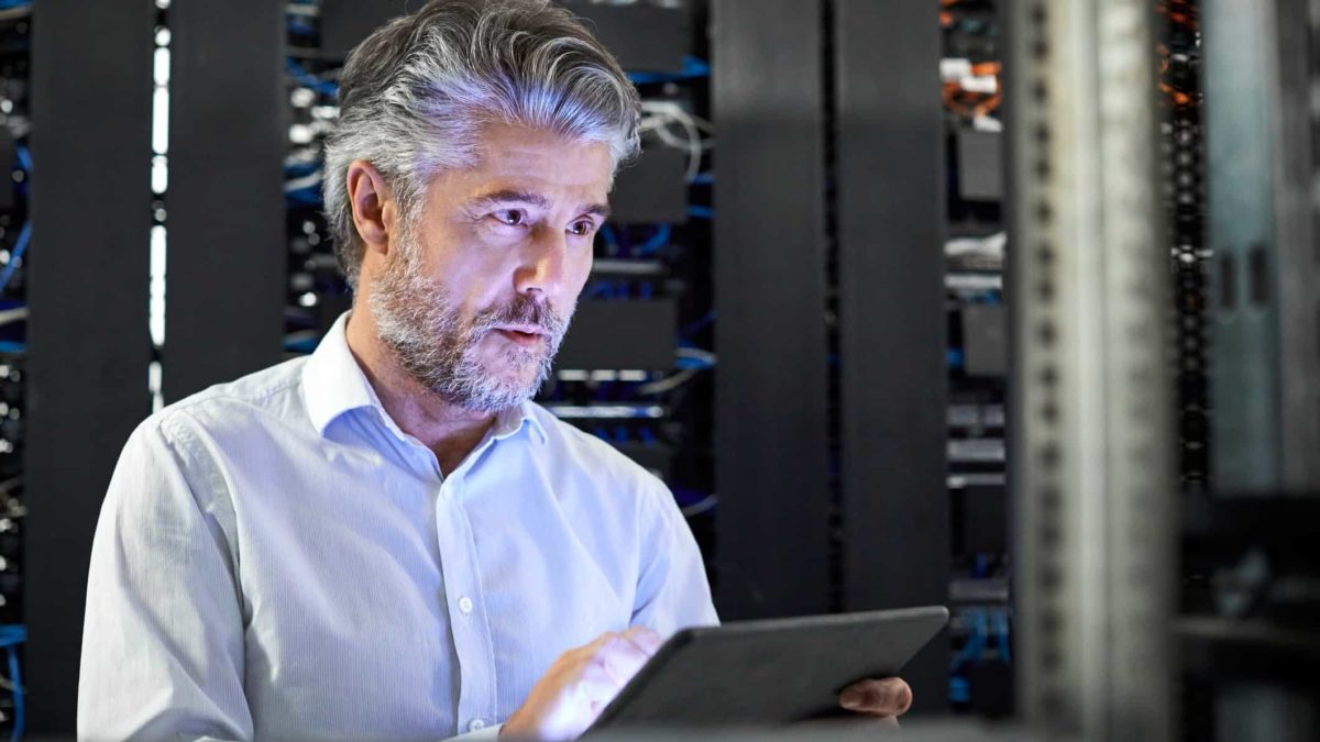 Cybersecurity professional man inspects server room and works on ipad