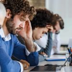 Group of entrepreneurs feeling frustrated during a meeting in the office. Focus is on man with headache.