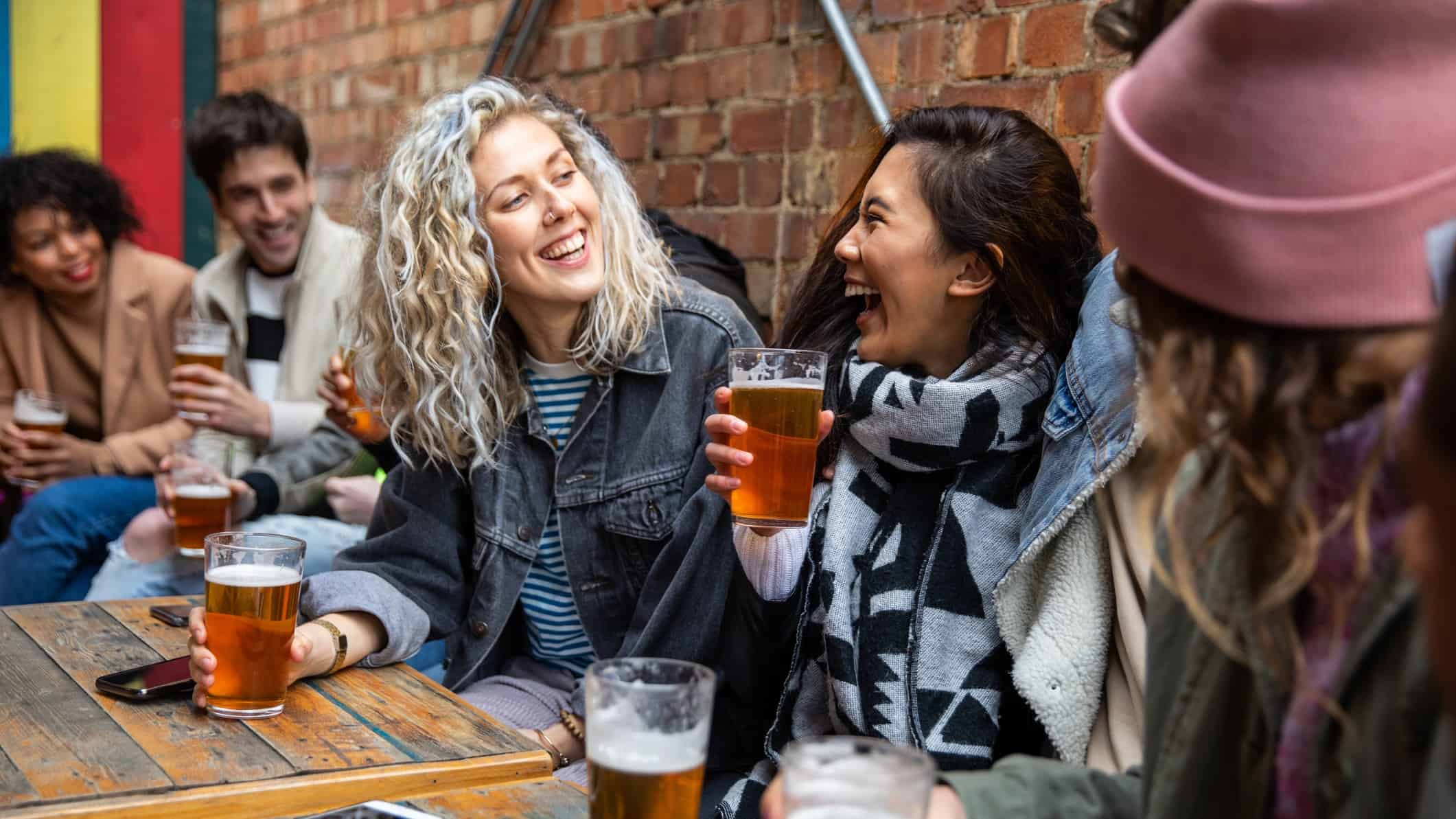 Two female friends laugh while drinking beer at a pub