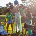 A group of eco warrior children together in nature wear green and capes and hold up a globe of the world..